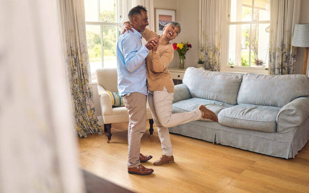 Love, funny and dance with a senior couple in the living room of their home together for bonding. Marriage, retirement or romance with an elderly man and woman laughing in the lounge of their house.